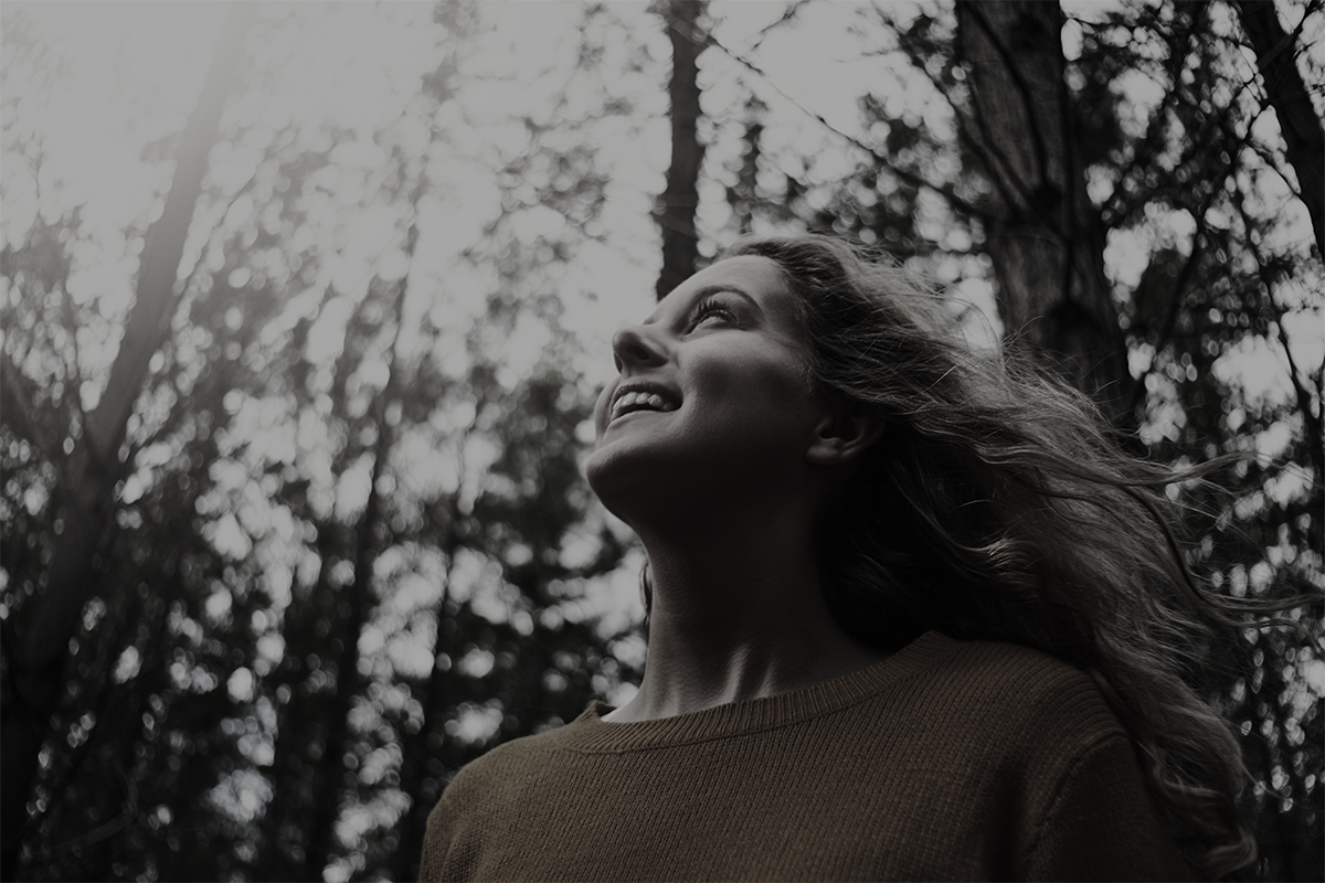Low angle view of a smiling pretty blonde young woman looking up in the forest